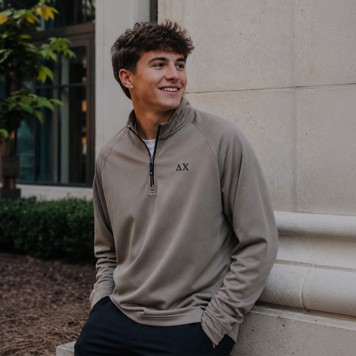College-aged man wearing the Mushroom Cutter & Buck Adapt quarter-zip with black embroidered Delta Chi Greek letters outdoors on campus.
