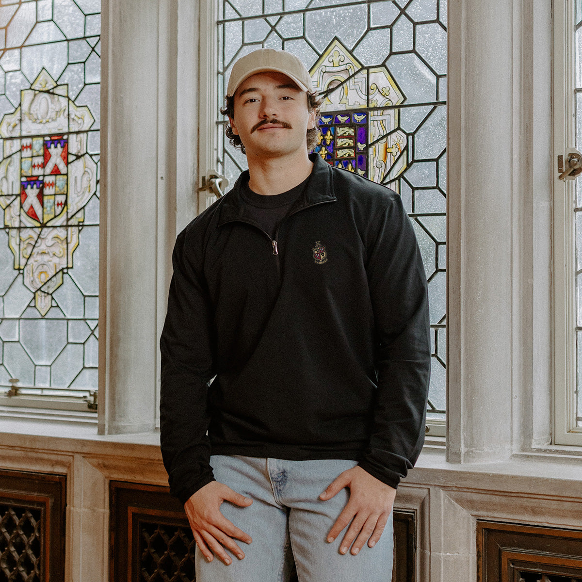 Male model wearing the black Delta Chi Embroidered Luxe Quarter Zip in front of stained glass windows with fraternity crests.